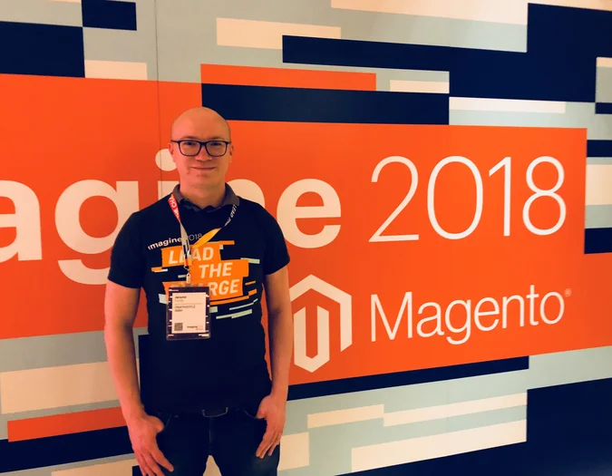 CEO Jaromir posing in front of an orange "Imagine 2018 Magento" event wall, wearing a matching "Lead the Charge" T-shirt