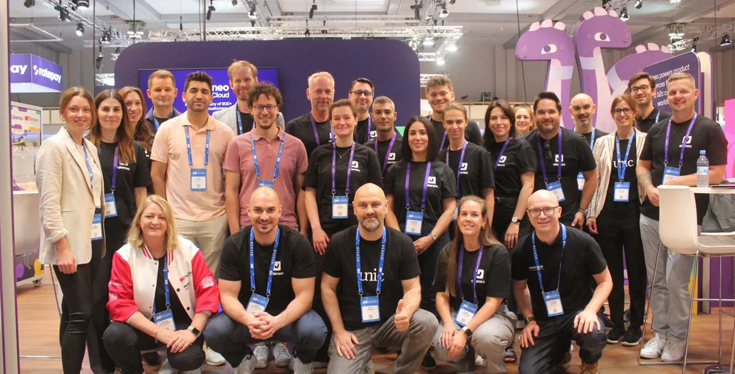 Large group of team members posing at an Akeneo event booth with purple branding and dinosaur figures