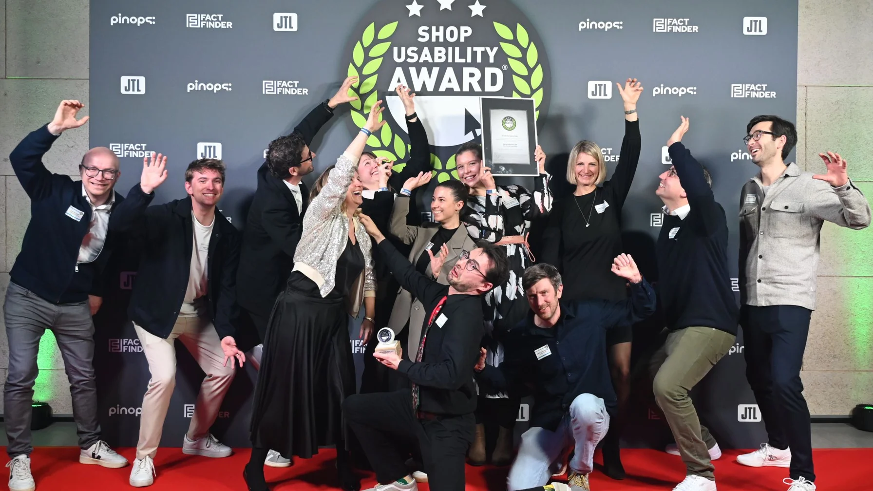 A group of people celebrating on a red carpet with an award, under a "Shop Usability Award" banner.