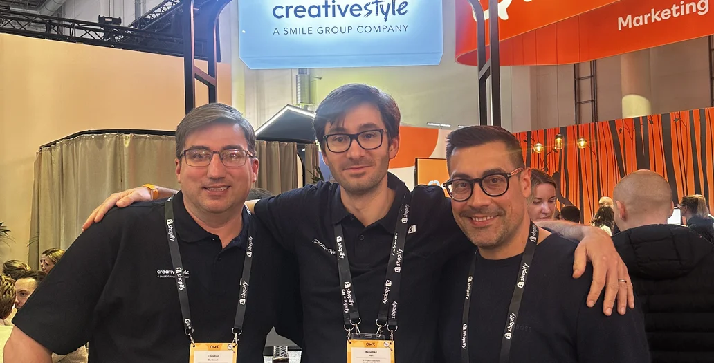 Three team members posing with arms around each other at a trade show booth with creative style branding during OMR Festival