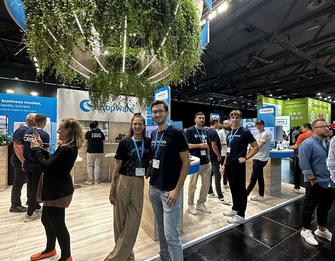 Team members at a large Shopware trade show booth decorated with hanging plants and creative style branding