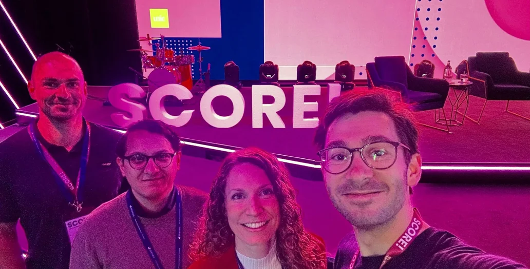 Four team members posing at the SCORE! event with purple lighting and stage branding