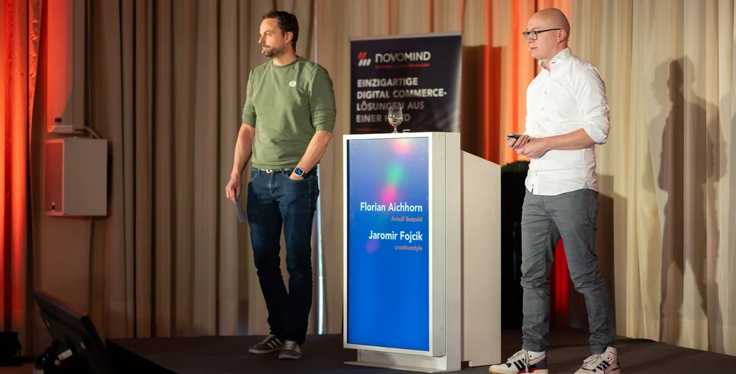 Two speakers, Florian Aichhorn and Jaromir Fojcik, presenting on a stage next to a digital lectern with novomind branding