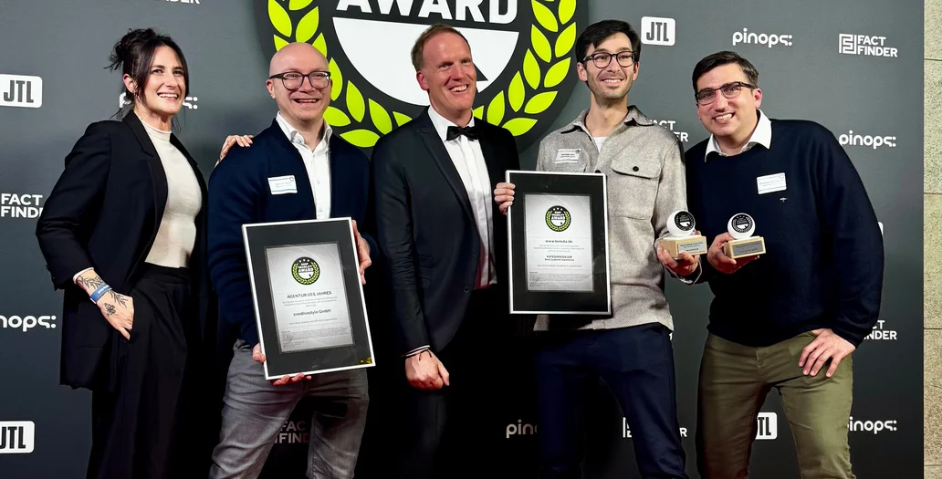 Five people smiling and holding awards on a red carpet, standing in front of a backdrop that reads "Shop Usability Award."