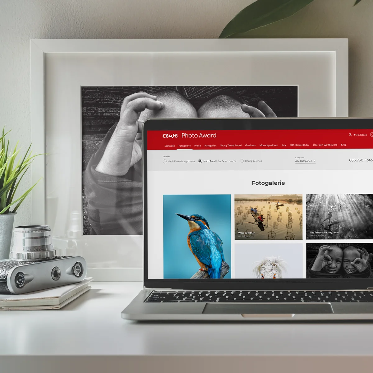 CEWE e-commerce website preview on a laptop showcasing the "CEWE Photo Award" gallery with various prize-winning photographs, set against a desk background with a framed black-and-white photo and a vintage camera