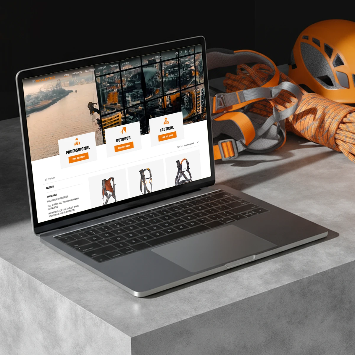 SKYLOTEC e-commerce website preview on a laptop showcasing industrial and outdoor safety sectors, featuring categories like "PROFESSIONAL", "OUTDOOR", and "TACTICAL" alongside safety gear in a workshop setting