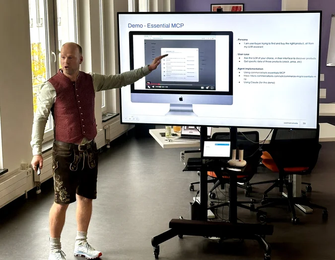 Man in traditional Bavarian lederhosen giving a presentation on "Essential MCP" via a large screen
