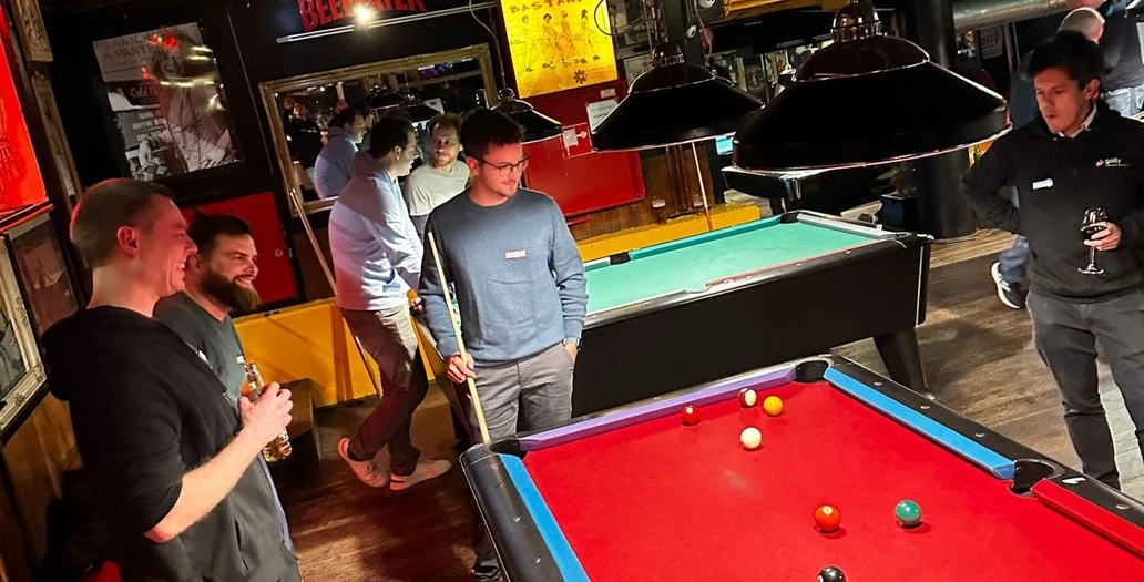 Group of people playing pool at a bar with a red pool table