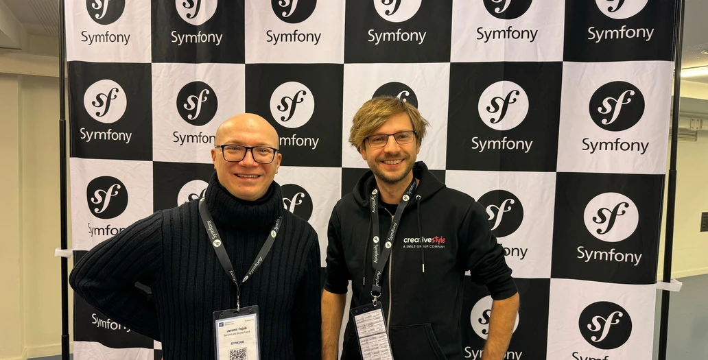 Two men posing in front of a black and white checkered Symfony logo backdrop