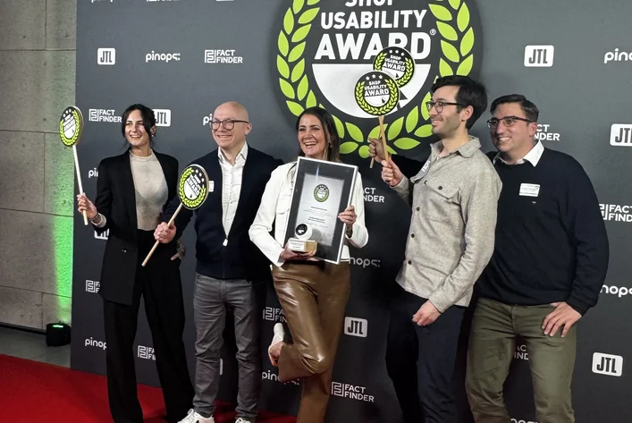 Five people posing on a red carpet, holding a plaque and tennis rackets, in front of a backdrop with "Shop Usability Award" logo.