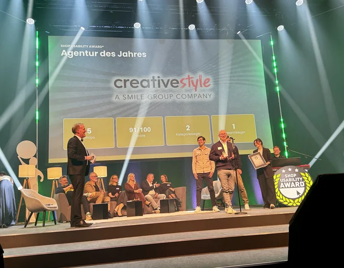 People on stage receiving an award for "Agentur des Jahres" from SCD; the background displays scores and achievements.