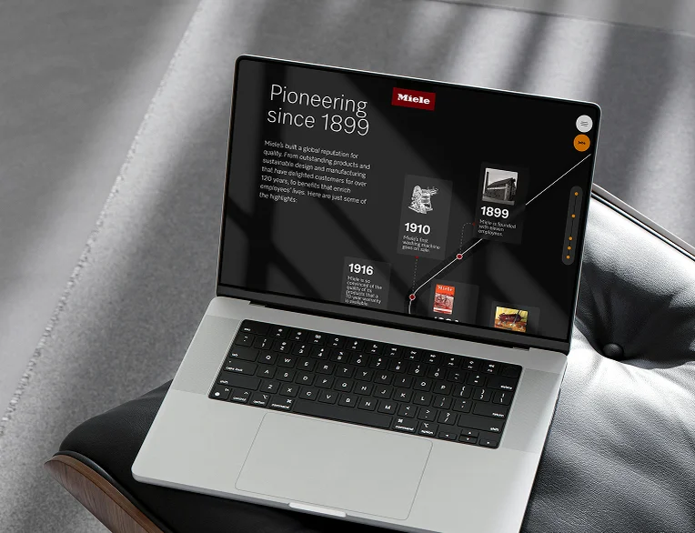 Miele X e-commerce website preview on a laptop showcasing a "Pioneering since 1899" brand history timeline, featuring milestones like the first washing machine from 1910, set against a dark background in a premium interior setting