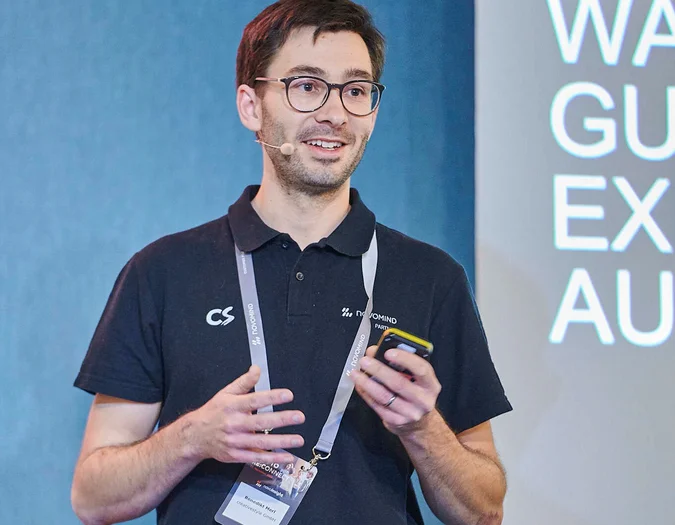 Man giving a presentation with a headset and smartphone in hand, wearing a novomind partner polo shirt