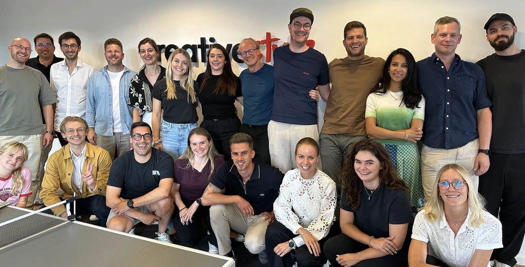 Large group of team members posing together in an office with a ping pong table in the foreground